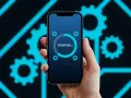 Dłoń trzyma smartfon z ekranem pokazującym pasek postępu "UPDATING..." i ikonki kół zębatych. Tło to schematyczne, neonowe koła zębate.