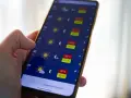 Dłoń trzyma smartfon z otwartą aplikacją pogoda, pokazującą prognozę z wysokimi temperaturami.