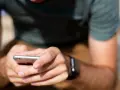 Mężczyzna z zegarkiem na ręku korzysta z telefonu, ucząc się, jak sparować zegarek z telefonem.