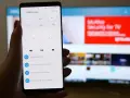 Smartfon z aplikacją do sterowania TV, umożliwiający screen mirroring. Na ekranie telefonu widoczny pilot, a na telewizorze reklama McAfee.