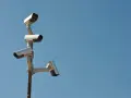 Cztery kamery monitoringu na słupie, czujne oko inwigilacji wpatrujące się w błękitne niebo.