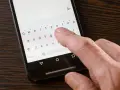 Dłoń naciska klawisz "Polski" na klawiaturze ekranowej smartfona.