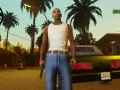 Postać z GTA San Andreas w białej koszulce i niebieskich jeansach, z pistoletem w ręku, na tle dzielnicy mieszkalnej.