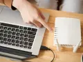 Dłoń wskazująca na router Wi-Fi podłączony do laptopa.