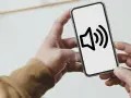 Dłoń trzyma smartfon z ikoną głośnika na ekranie.