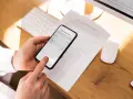 Ręce trzymają smartfon, który działa jak skaner dokumentów, skanując polisę ubezpieczeniową leżącą na biurku.