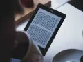 Osoba czyta książkę w formacie kindle. Na ekranie widoczny jest tekst powieści.