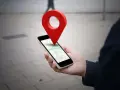 Dłoń trzyma smartfon z mapą, a nad nim unosi się czerwona pinezka. To wizualizacja, jak wysłać pinezkę z lokalizacją.