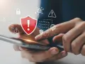 Dłonie trzymające smartfon, nad którym wyświetlają się ikony symbolizujące bezpieczeństwo i zagrożenia. Skuteczny antywirus na telefon chroni przed wirusami i atakami.