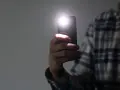 Dłoń trzyma smartfon z włączoną latarką.