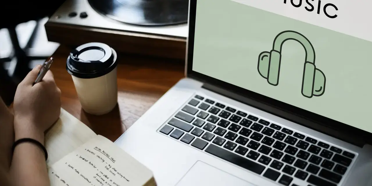 Osoba notuje pomysły na biznes, słuchając muzyki przez słuchawki. Laptop wyświetla ikonę słuchawek i napis "Music", sugerując rozpoznawanie muzyki.