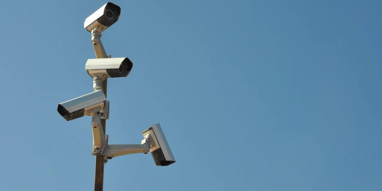 Cztery kamery monitoringu na słupie, czujne oko inwigilacji wpatrujące się w błękitne niebo.