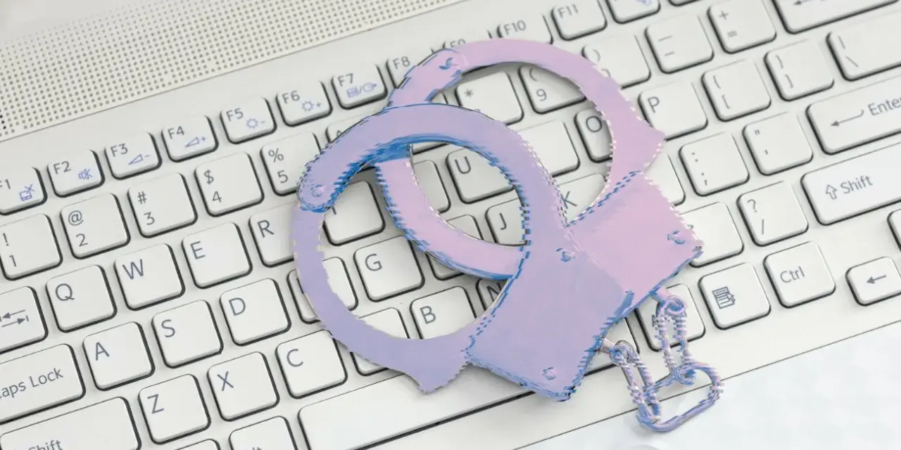 Różowe kajdanki leżą na białej klawiaturze laptopa.