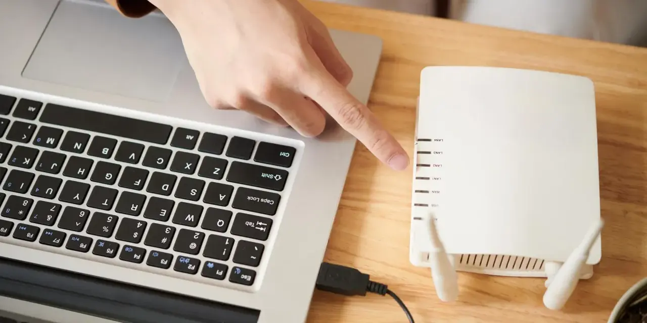 Dłoń wskazująca na router Wi-Fi podłączony do laptopa.