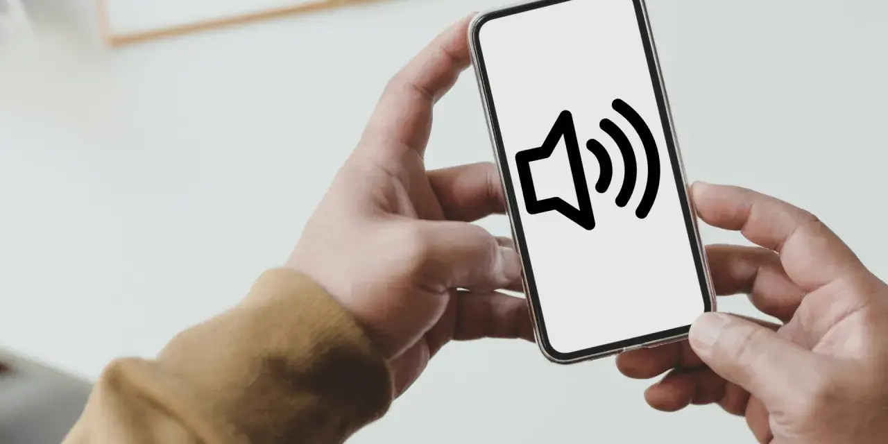 Dłoń trzyma smartfon z ikoną głośnika na ekranie.