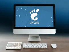 Komputer z logo GNOME, tablet i klawiatura na drewnianym biurku.