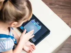 Dziecko dotyka ekranu tabletu z ikonami aplikacji społecznościowych, w tym Facebooka. Ciekawe, od ilu lat jest Facebook?