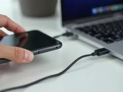 Dłoń trzyma telefon, który jest podłączony kablem USB do laptopa. Prosty sposób, jak połączyć telefon z laptopem.