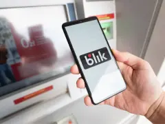 Dłoń trzyma smartfon z logo Blik. Czy Blik jest tylko w Polsce? Płatność zbliżeniowa przy bankomacie.