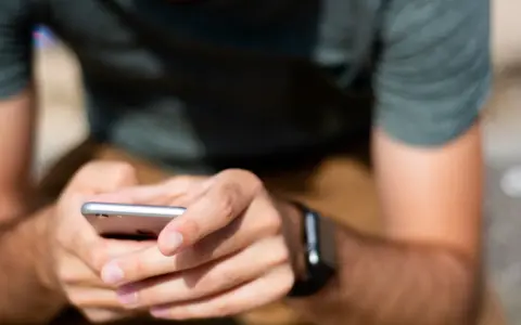 Mężczyzna z zegarkiem na ręku korzysta z telefonu, ucząc się, jak sparować zegarek z telefonem.