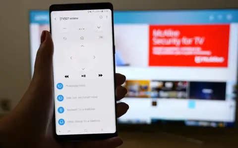 Smartfon z aplikacją do sterowania TV, umożliwiający screen mirroring. Na ekranie telefonu widoczny pilot, a na telewizorze reklama McAfee.
