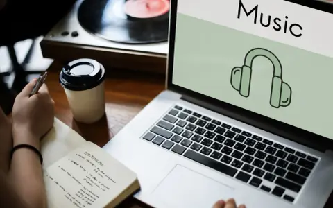 Osoba notuje pomysły na biznes, słuchając muzyki przez słuchawki. Laptop wyświetla ikonę słuchawek i napis "Music", sugerując rozpoznawanie muzyki.