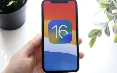 Dłoń trzyma iPhone'a z ikoną iOS 16 na kolorowej tapetcie.
