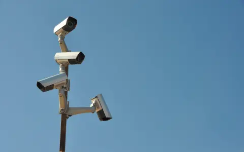 Cztery kamery monitoringu na słupie, czujne oko inwigilacji wpatrujące się w błękitne niebo.