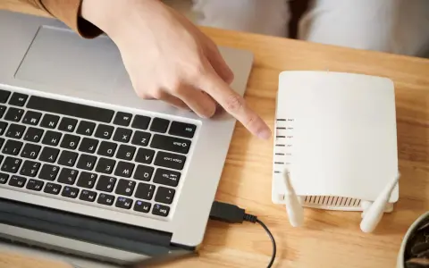 Dłoń wskazująca na router Wi-Fi podłączony do laptopa.