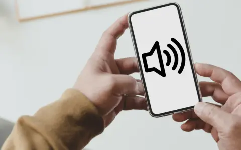 Dłoń trzyma smartfon z ikoną głośnika na ekranie.
