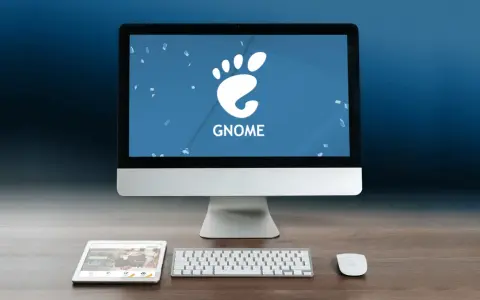 Komputer z logo GNOME, tablet i klawiatura na drewnianym biurku.