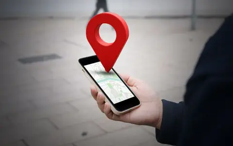 Dłoń trzyma smartfon z mapą, a nad nim unosi się czerwona pinezka. To wizualizacja, jak wysłać pinezkę z lokalizacją.