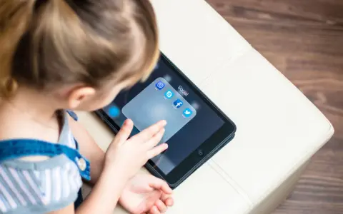 Dziecko dotyka ekranu tabletu z ikonami aplikacji społecznościowych, w tym Facebooka. Ciekawe, od ilu lat jest Facebook?