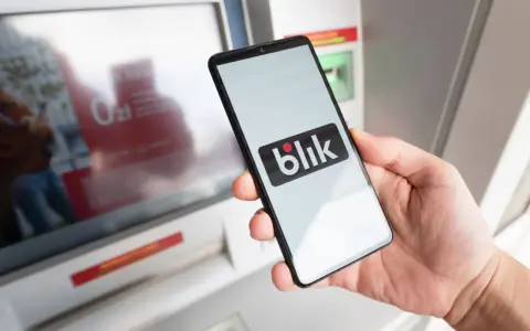 Dłoń trzyma smartfon z logo Blik. Czy Blik jest tylko w Polsce? Płatność zbliżeniowa przy bankomacie.