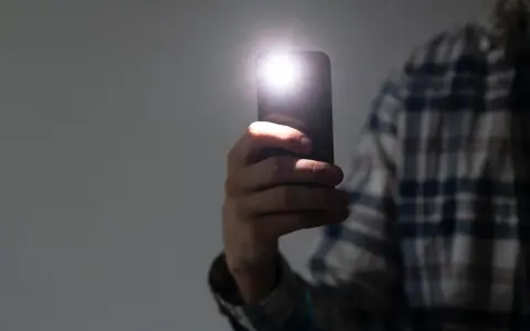 Dłoń trzyma smartfon z włączoną latarką.