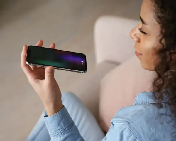Kobieta trzyma telefon, na ekranie którego widać ikonę mikrofonu, sugerującą aplikację do nagrywania rozmów.