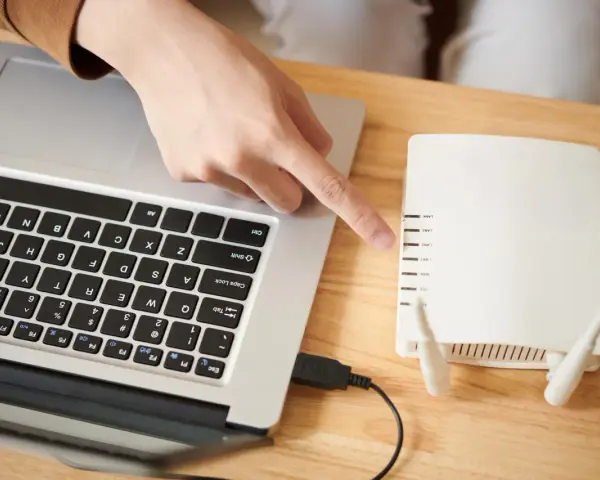 Dłoń wskazująca na router Wi-Fi podłączony do laptopa.