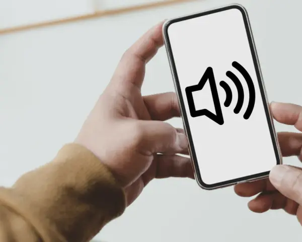 Dłoń trzyma smartfon z ikoną głośnika na ekranie.
