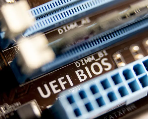 Zbliżenie na płytę główną z widocznym napisem "UEFI BIOS" i złączami RAM. W tle widać oznaczenie DIMM_A1, a poniżej DIMM_B1. Ten układ jest kluczowy dla bezpieczeństwa systemu, podobnie jak moduł **TPM 2.0**.