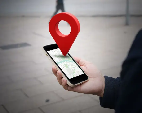 Dłoń trzyma smartfon z mapą, a nad nim unosi się czerwona pinezka. To wizualizacja, jak wysłać pinezkę z lokalizacją.