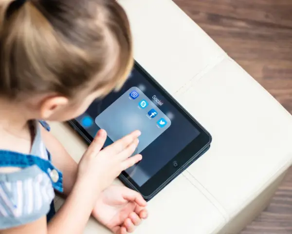 Dziecko dotyka ekranu tabletu z ikonami aplikacji społecznościowych, w tym Facebooka. Ciekawe, od ilu lat jest Facebook?