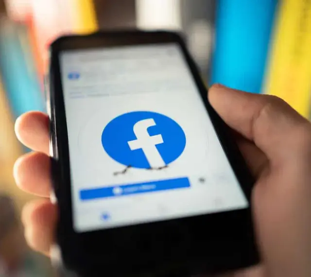 Dłoń trzyma smartfon z logo Facebooka. Chcesz wiedzieć, jak usunąć FB?