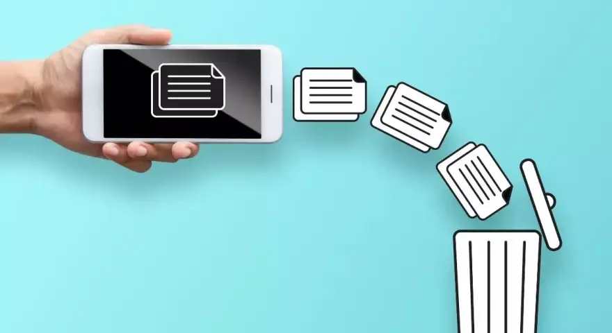 Dłoń trzyma telefon, z którego wypadają dokumenty prosto do kosza. Tak właśnie działa kosz w telefonie, gdy usuwasz pliki.