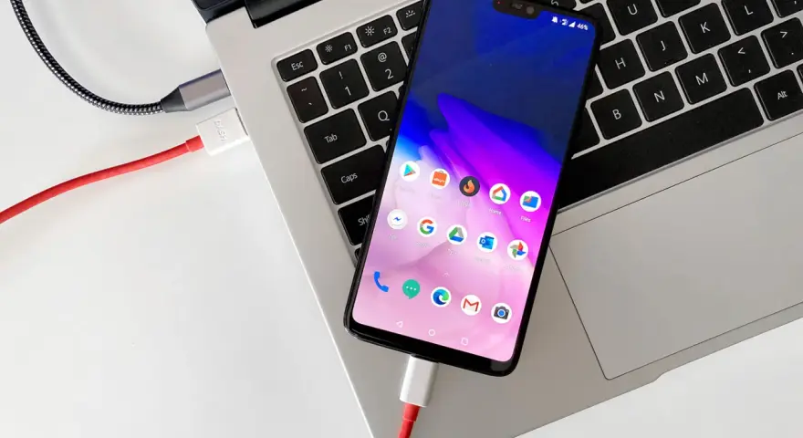 Smartfon podłączony kablem do laptopa, gotowy do przenoszenia zdjęć.