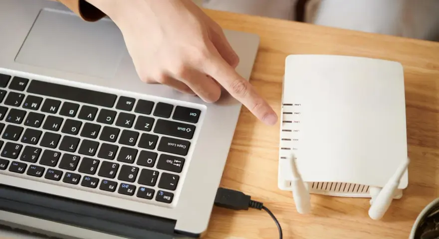Dłoń wskazująca na router Wi-Fi podłączony do laptopa.