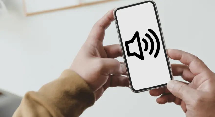 Dłoń trzyma smartfon z ikoną głośnika na ekranie.