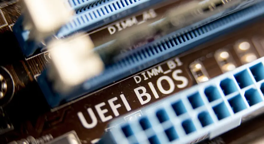 Zbliżenie na płytę główną z widocznym napisem "UEFI BIOS" i złączami RAM. W tle widać oznaczenie DIMM_A1, a poniżej DIMM_B1. Ten układ jest kluczowy dla bezpieczeństwa systemu, podobnie jak moduł **TPM 2.0**.