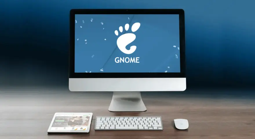 Komputer z logo GNOME, tablet i klawiatura na drewnianym biurku.