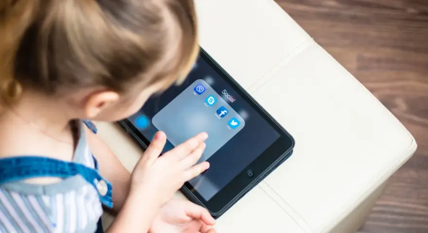 Dziecko dotyka ekranu tabletu z ikonami aplikacji społecznościowych, w tym Facebooka. Ciekawe, od ilu lat jest Facebook?