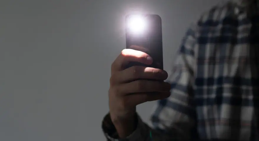 Dłoń trzyma smartfon z włączoną latarką.